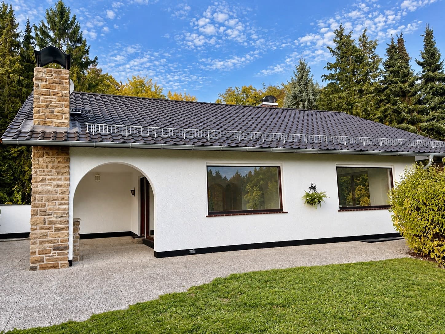 Weiße Hausfassade mit großen Fenstern und überdachter Rundbogenveranda