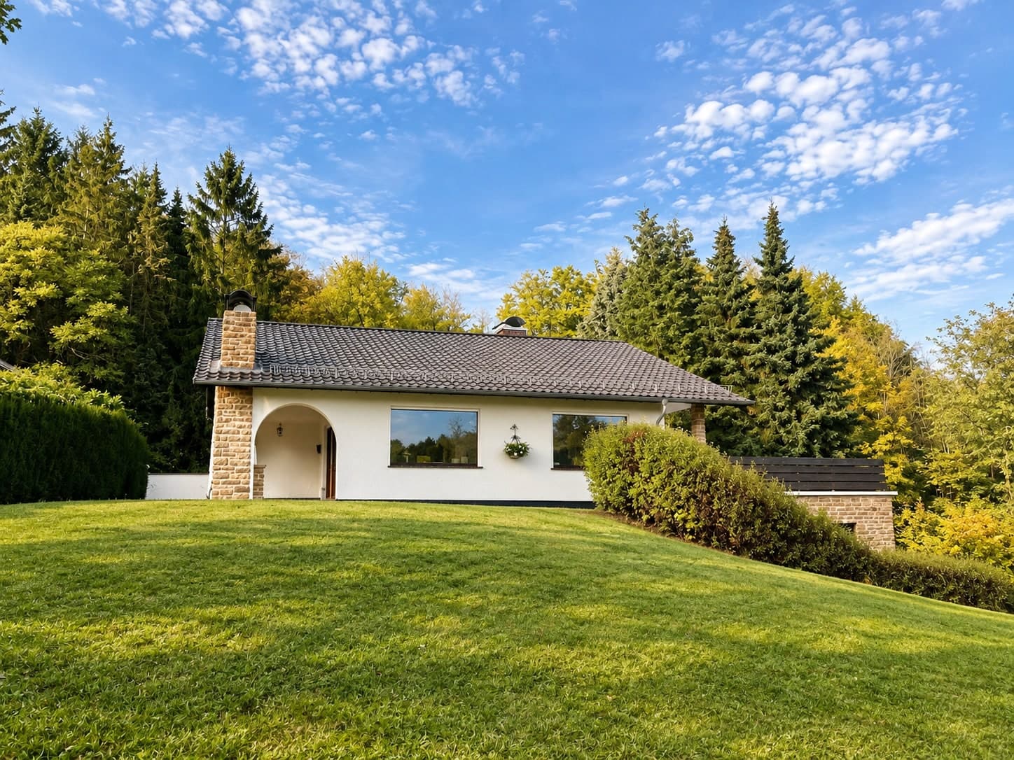 Haus hinter einer Rasenfläche zwischen hohen Bäumen