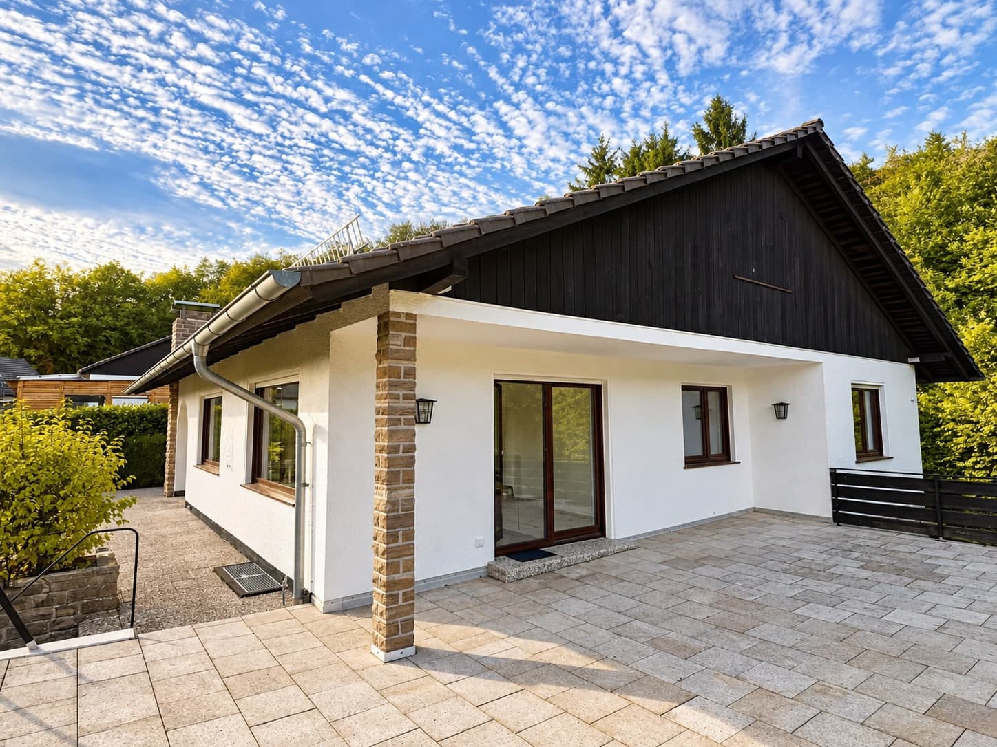 Haus mit dunklem Giebel und Natursteinsäule von der Terrasse aus