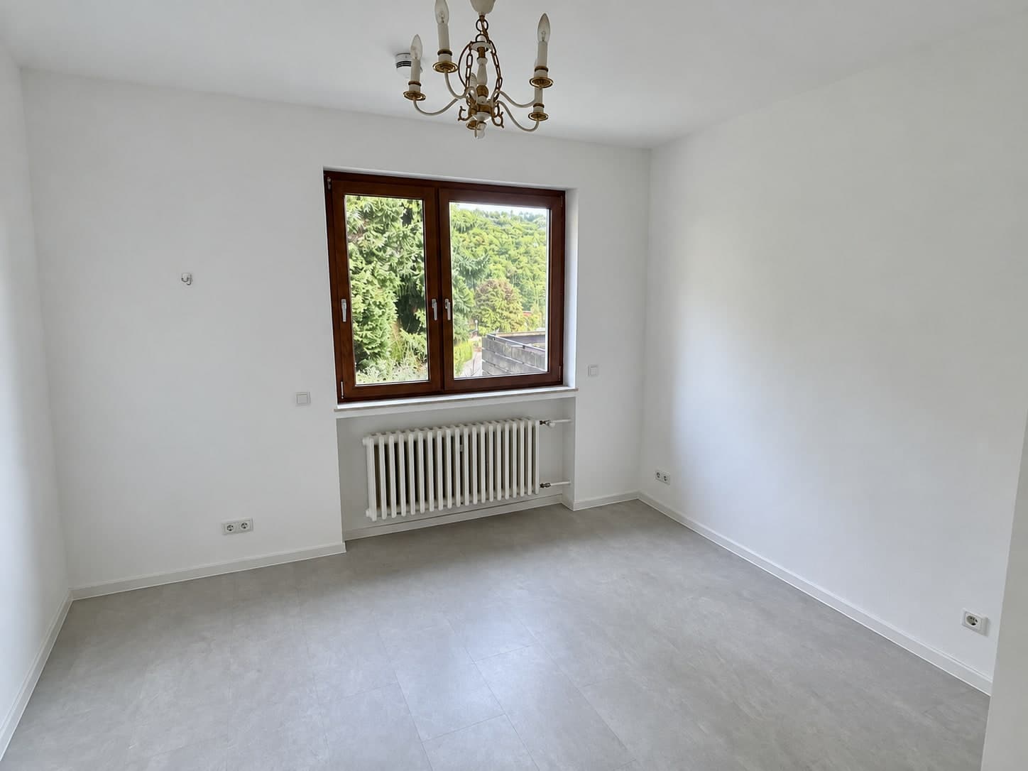 Leerer heller Raum mit Kronleuchter, Holzfenster und Heizkörper