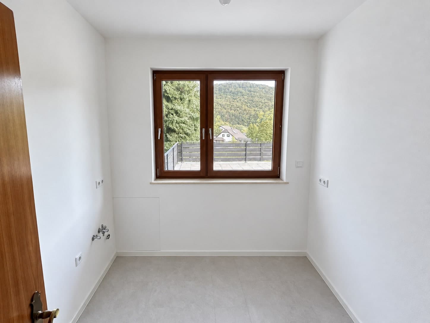 Schmaler leerer Raum mit Wasseranschlüssen links und Fenster zur Terrasse