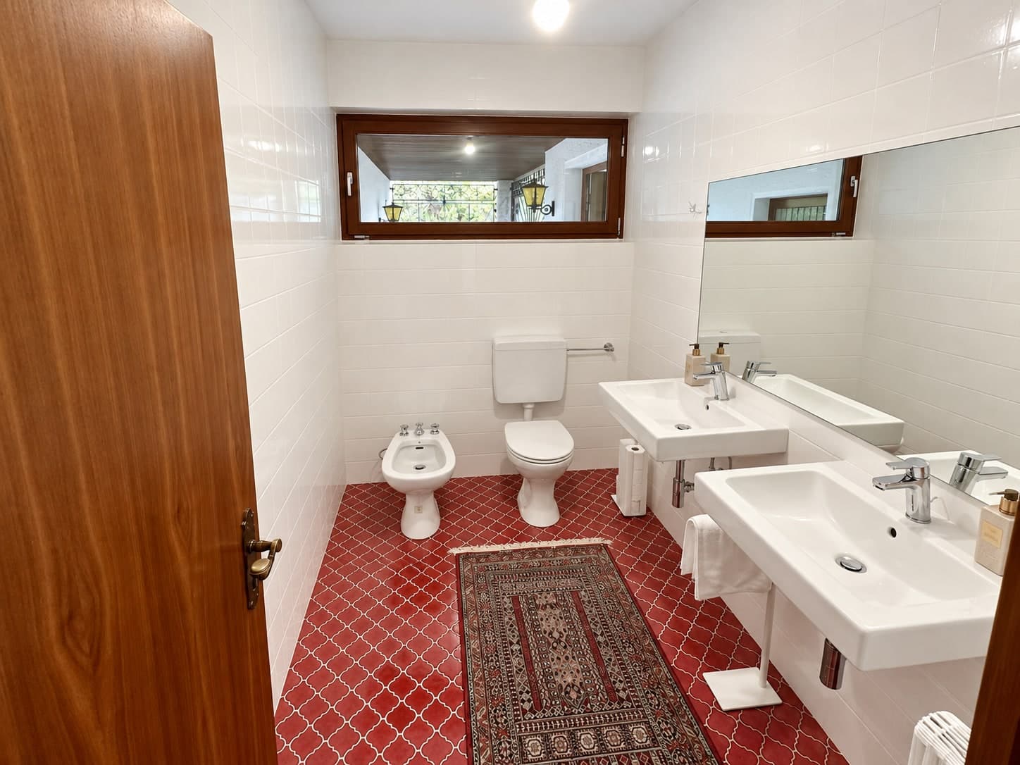 Badezimmer mit zwei Waschbecken, Toilette, Bidet und roten Bodenfliesen