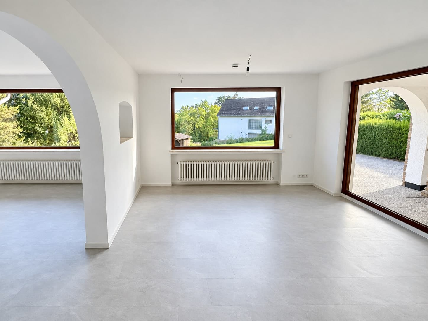 Heller Wohnbereich mit Rundbogen, großem Fenster und Zugang zur Veranda