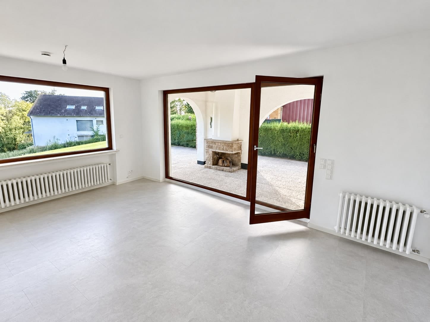 Wohnbereich mit Eckfenster und geöffneter Glastür zum Außenkamin
