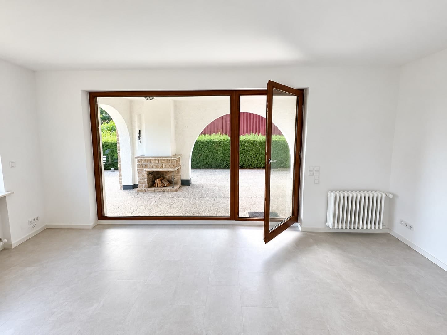 Große Glasfront mit geöffneter Tür und Blick auf den steinernen Außenkamin