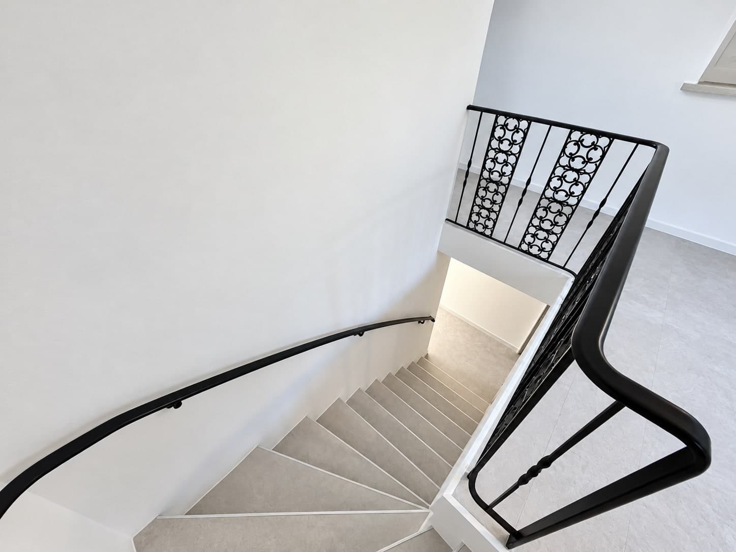 Blick von oben auf die helle Treppe mit schwarzem Handlauf und Ziergeländer