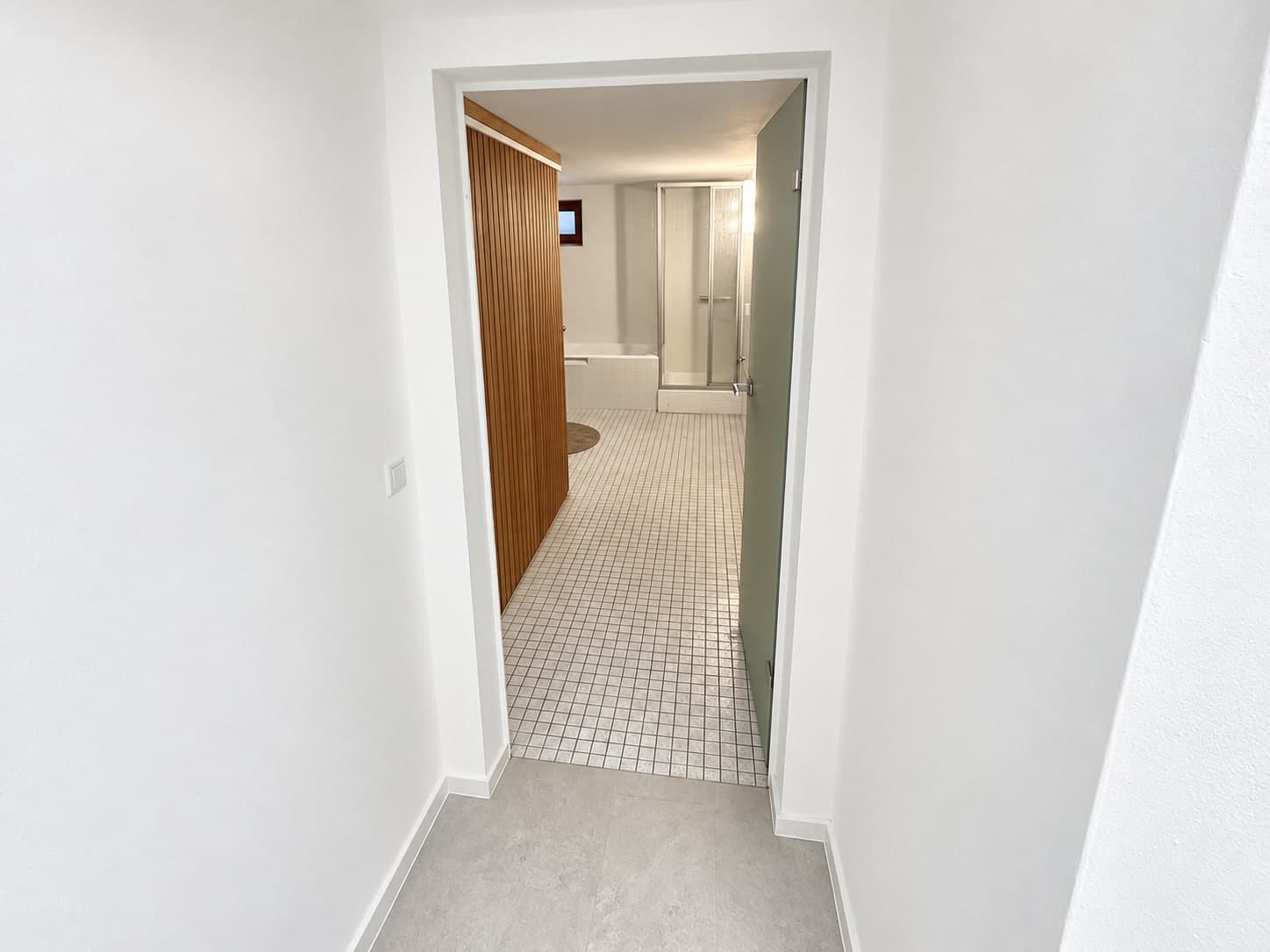 Blick durch den Flur in das geflieste Bad mit Saunawand, Wanne und Dusche
