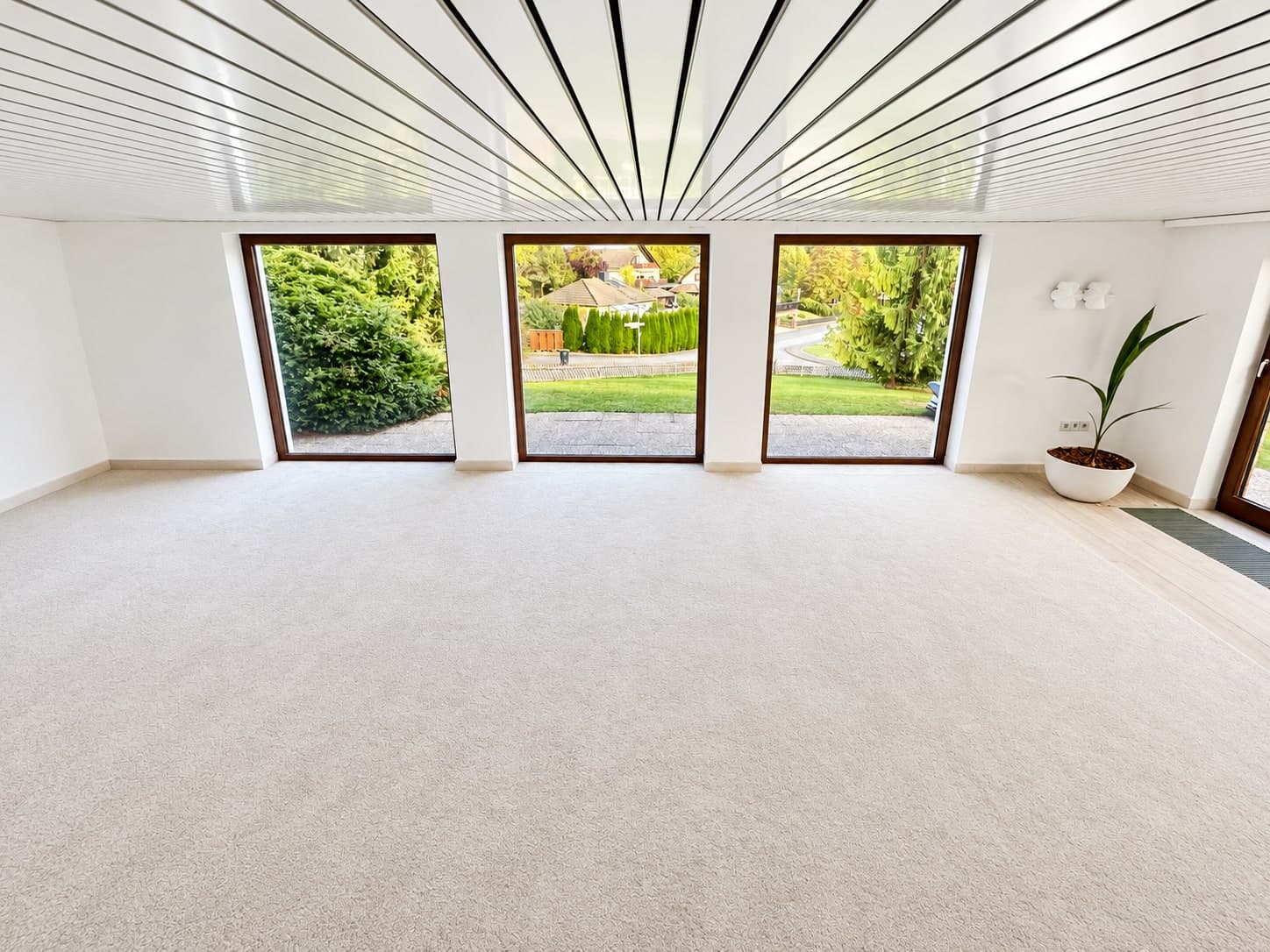 Großer Raum mit hellem Teppich, Paneeldecke und drei bodentiefen Fenstern