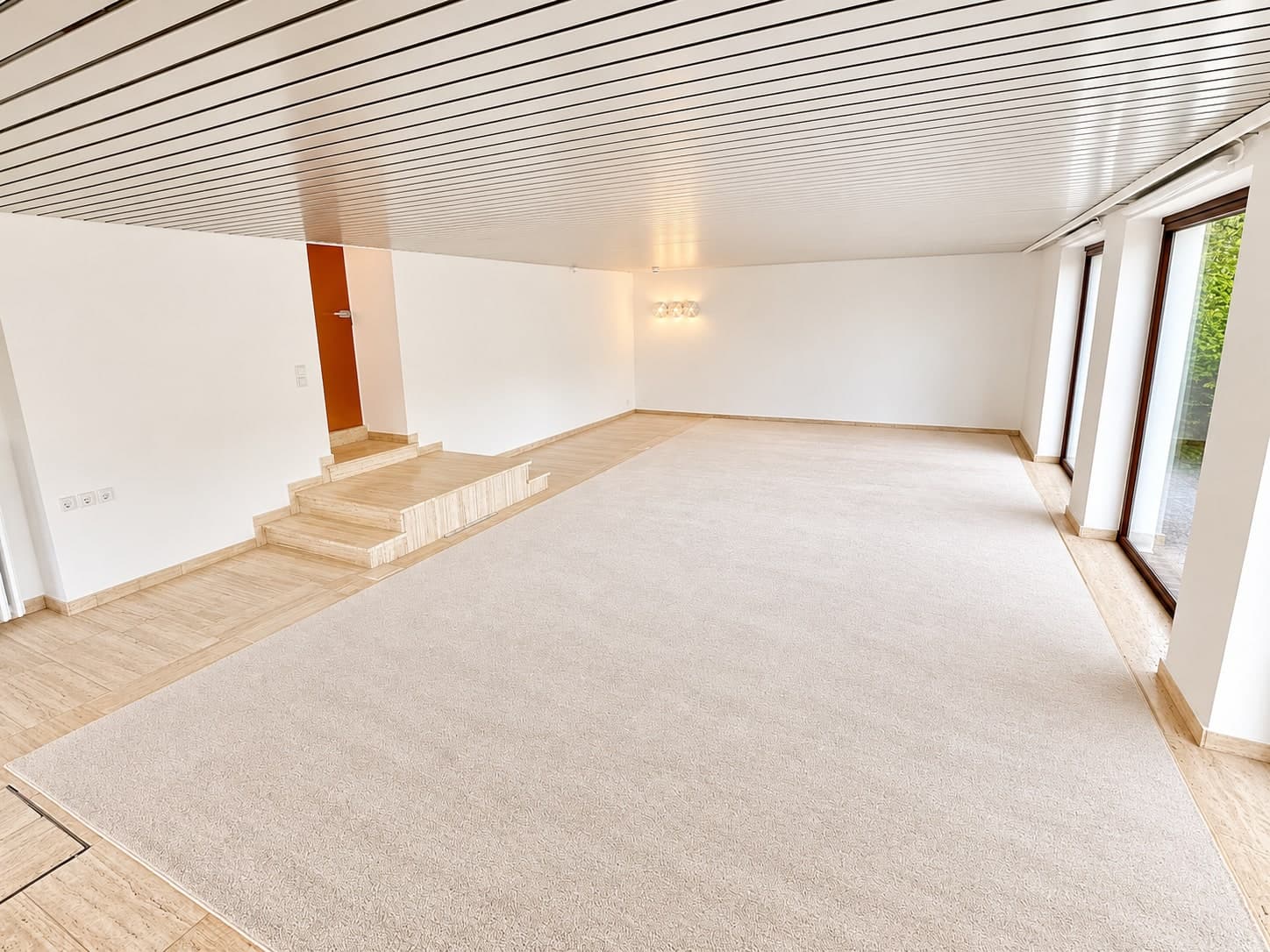 Großer heller Raum mit Teppichfläche, Steinstufen und Paneeldecke